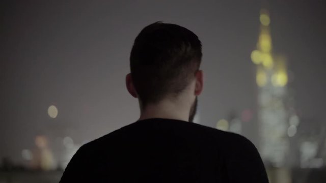 Man walking towards skyline in rain at night
