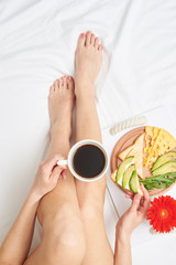 Obraz na płótnie Canvas Slim girl tasting coffee while relaxing in bed