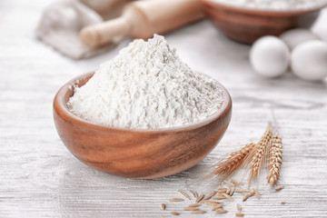 Bowl of white flour and wheat ears on wooden table