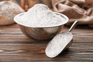 Metal bowl and scoop full of white flour on wooden table