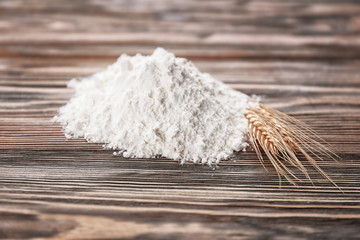 Heap of white flour and wheat ears on wooden table