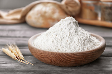 Fototapeta na wymiar Flat bowl of white flour and wheat ears on wooden table