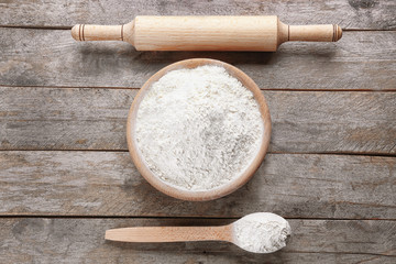 Bowl of white flour, spoon and roller pin on grey wooden background