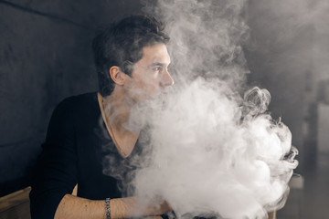 Vaping man holding a mod. A cloud of vapor. Black background. Smoking electronic cigarette Vape advertisement concept