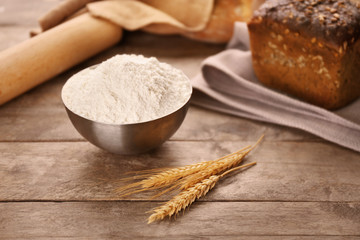 Bowl of white flour and wheat ears on wooden table