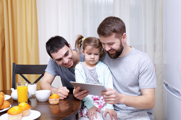 Male gay couple with daughter having breakfast in kitchen