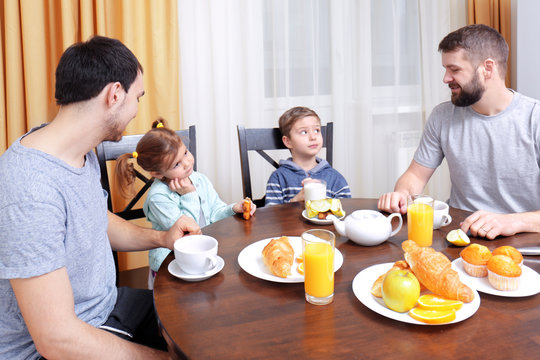 Male gay couple with children having breakfast in kitchen