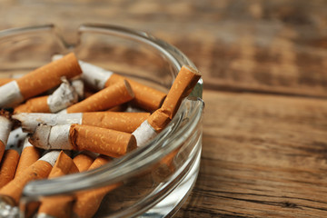 Cigarette butts in ashtray on wooden background