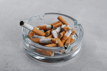 Cigarette butts in ashtray on light background