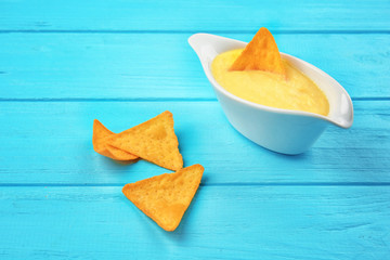 Gravy boat with tasty cheese sauce and snack on color wooden background