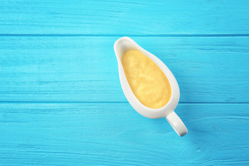 Gravy boat with tasty cheese sauce on color wooden background