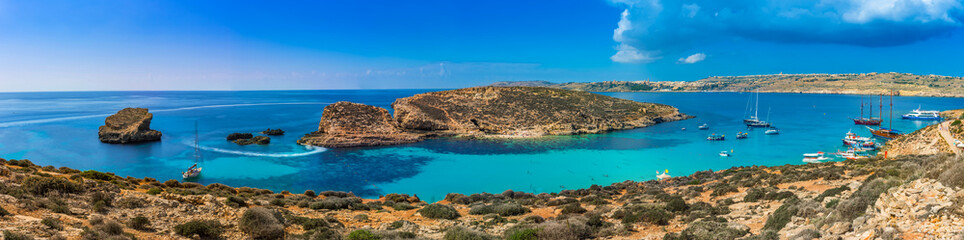 Comino, Malta - Panoramic skyline view of the  beautiful Blue Lagoon on the island of Comino with sailboats, traditional Luzzu boats and tourists enjoying the mediterranean sea - obrazy, fototapety, plakaty