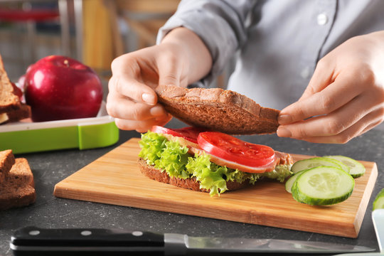 Mother preparing sandwich for school lunch on table