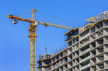 Fototapeta na wymiar Construction site. Construction crane and high-rise building under construction against blue sky.