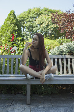 A young woman sitting on a park bench eating an apple