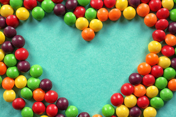 Colorful candies in shape of heart on color background