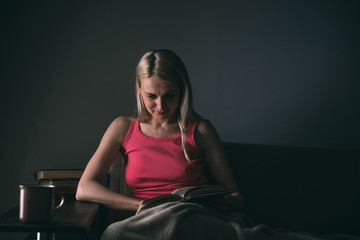 Girl enthusiastically reading a book best-selling house under a rug on a comfortable sofa with a lamp