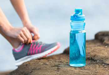 Exercise and drinking water concept. Bottle of water next to runner tying shoes. 