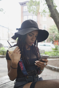 Young woman holding coffee while using smartphone outdoors