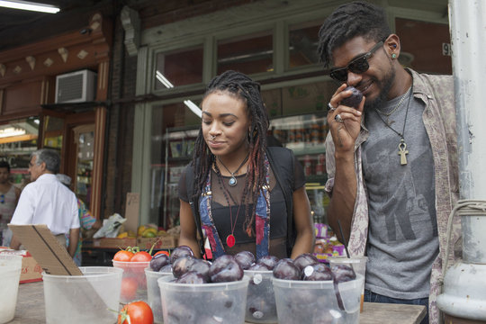 A young man and woman at a fruit stall. 