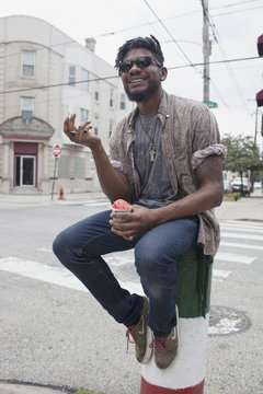 Smiling young man holding ice cream while sitting on bollard