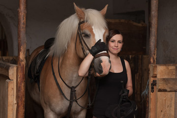 Young woman hugging her horse in stable.