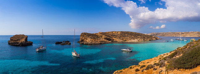 Comino, Malta - Panoramic skyline view of the  beautiful Blue Lagoon on the island of Comino with sailboats, traditional Luzzu boats and tourists enjoying the mediterranean sea