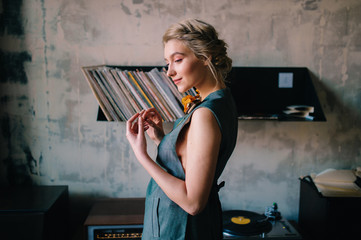 Portrait of young and attractive pensive model girl in beautiful dress relaxing and listening music in retro cafe with gramophone and loft style wall. Romantic, vintage and nostalgic lifestyle.