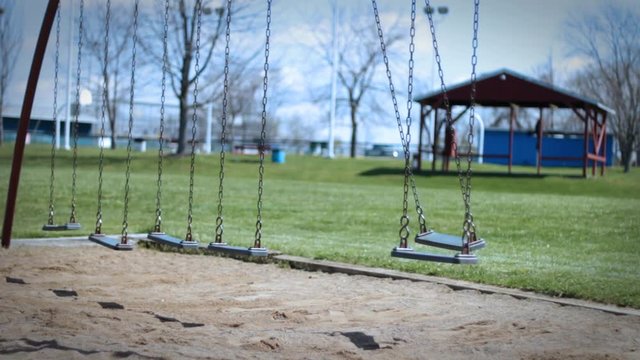 Child kidnapping concept - lonely swing flying in the wind in empty park during dreary day