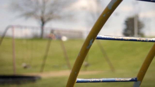 Close up of monkey bars on playground jungle gym with swings in background in daytime
