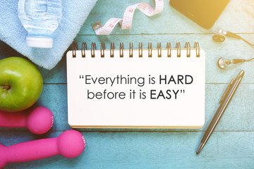 Fitness motivation quotes written on open notebook. Fitness equipment on wooden background.