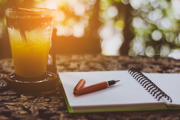 pen and fruit juice on the desk, open a blank white notebook on table