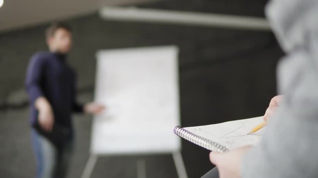 Closeup view of woman taking notes during the presentation. Handsome young businessman pointing at flipchart during presentation in conference room. Shot in 4k