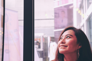Portrait image of a beautiful Asian woman staying in restaurant and looking outside window with smiley face