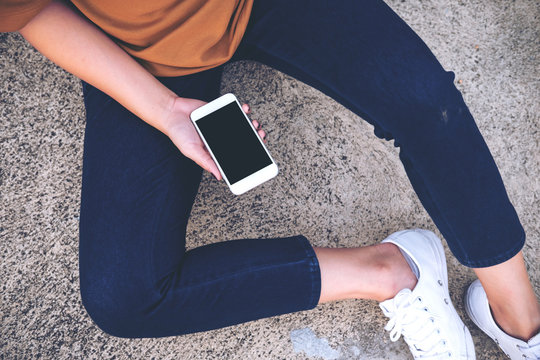 Mockup image of a woman sitting on the street and holding mobile phone with blank white screen   