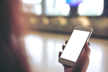 Mockup image of a woman holding and using white mobile phone with blank white screen while standing and waiting for baggage claim in the airport