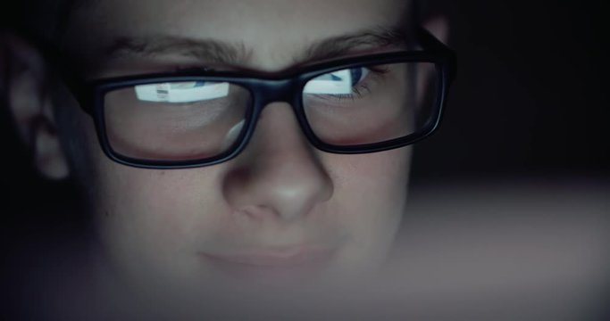 boy working at a computer in a dark room, surfing the Internet, close-up