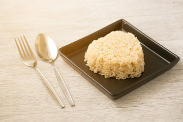 brown rice heart shape on black plate on wooden background