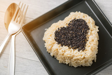 brown rice and black sesame heart shape on black plate on wooden background
