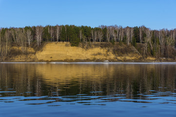 The steep bank of the river is reflected in the water surface of the river. Beautiful reflection of the shore in the water.