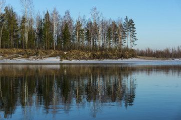 Fototapeta na wymiar Island in the snow reflected in the water. Spring landscape on the bank of the river Ob.