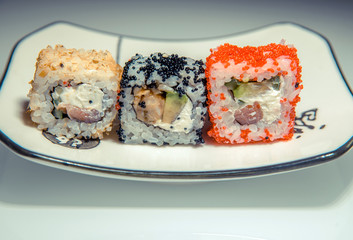 Three sushi on a white plate standing on the white glass 