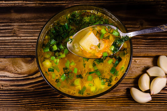 Vegetable soup in a glass bowl on wooden table. Spoon with soup. Top view