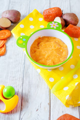 Food for kids, children's lure, organic puree from boiled potatoes and carrot in a bowl on a white rustic wooden background