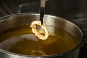 Lightly fried Calamari ring being taken out of a pan of hot oil.