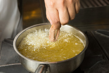 Calamari ring being placed into a pan of hot bubbling oil.