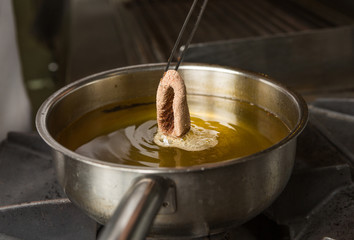 Calamari ring being placed into a pan of hot oil.