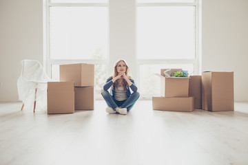 Dream come true! Portrait of young pretty woman sitting on the floor and thinking how to unpack all...