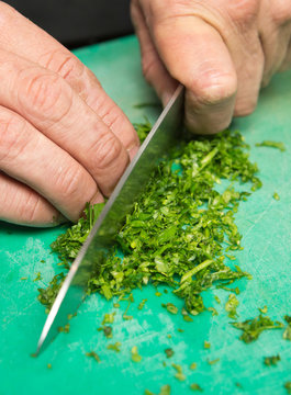 Organic fresh parsley being finely chopped on a green cutting board.