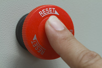Finger touch on red emergency stop switch button on control panel for machine control.
